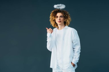 curly teenager in angel costume with halo above head showing thumb up isolated on green clipart