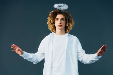 curly teenager in angel costume with halo above head and outstretched hands isolated on green clipart