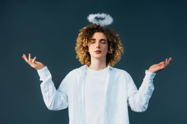 curly teenager in angel costume with halo above head, closed eyes and outstretched hands isolated on green clipart