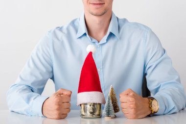 cropped view of man with clenched fists near glass jar with money and santa hat isolated on white  clipart