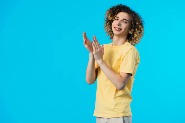 улыбающийся кудрявый подросток аплодирует изолированному на голубом
