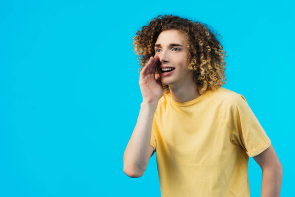 smiling curly teenager gossiping isolated on blue
