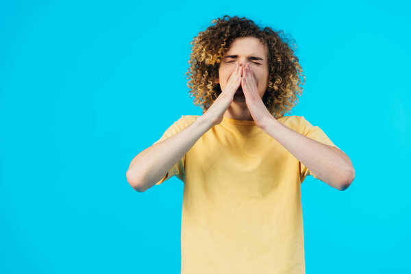 curly teenager sneezing with closed eyes  isolated on blue