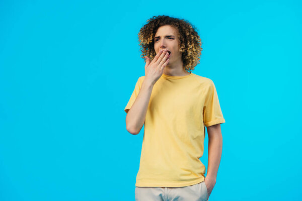 sleepy curly teenager yawning isolated on blue
