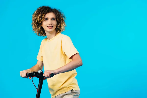Lächelnder Lockiger Teenager Fährt Elektroroller Und Schaut Isoliert Auf Blauem — Stockfoto