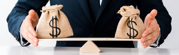 panoramic shot of businessman touching scales with money bags isolated on white 
