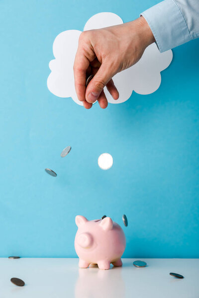 cropped view of man throwing coins near pink piggy bank on blue 