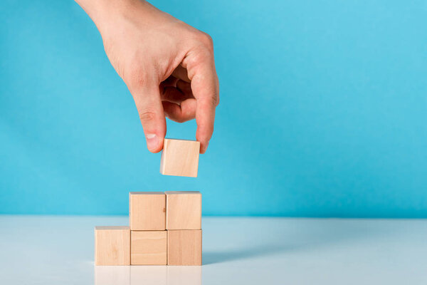 cropped view of man putting wooden cube on blue 