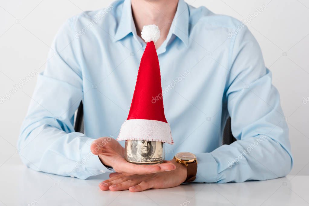 cropped view of businessman holding jar with dollar banknotes and santa hat isolated on white 