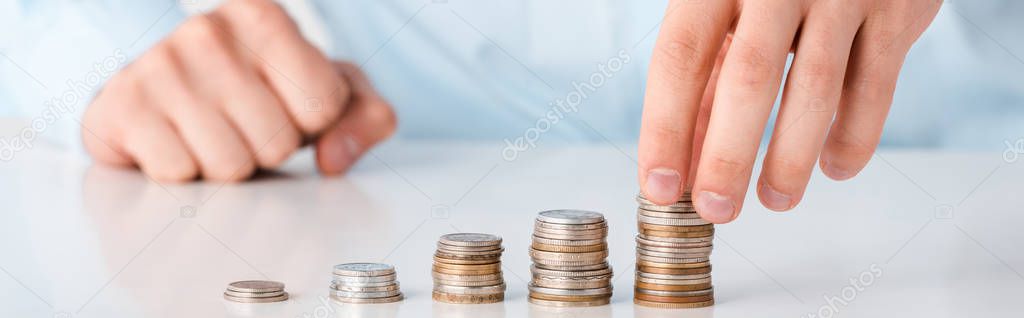 panoramic shot of man touching stack of coins isolated on white 