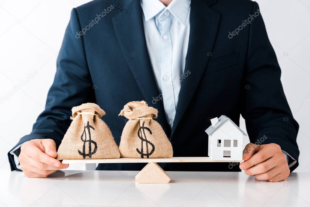 cropped view of businessman near scales with money bags and carton house isolated on white 