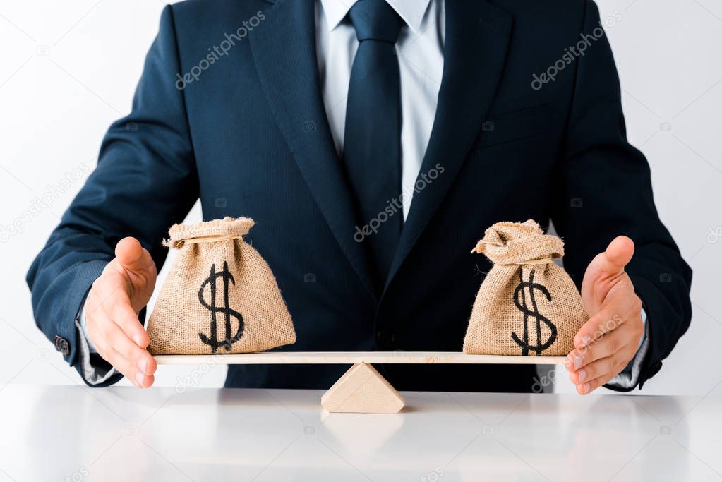 cropped view of businessman touching scales with money bags isolated on white 