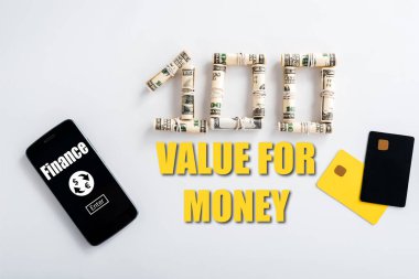 Para ruloları yakınındaki akıllı telefonun üst görünümü, para için değer mektupları ve beyaz kart şablonları 