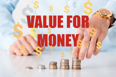 cropped view of man touching stack of coins near value of money letters and dollar signs on white  clipart