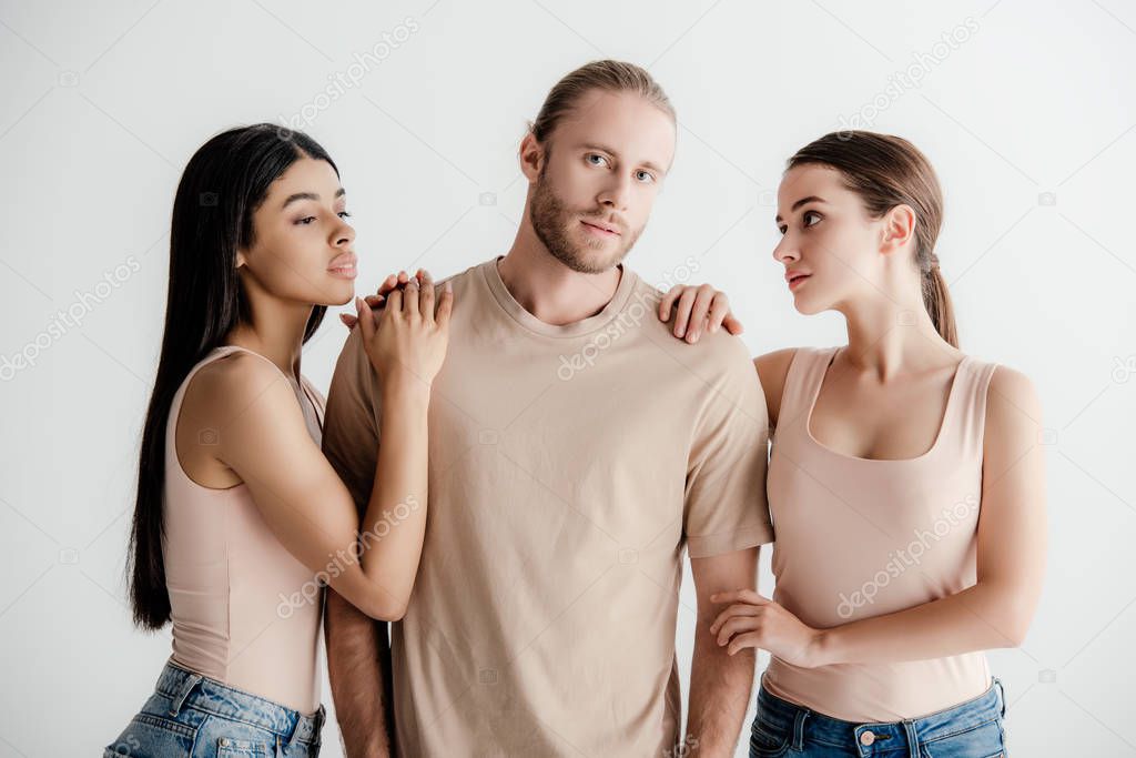 young multicultural women standing near handsome man in beige outfit isolated on white