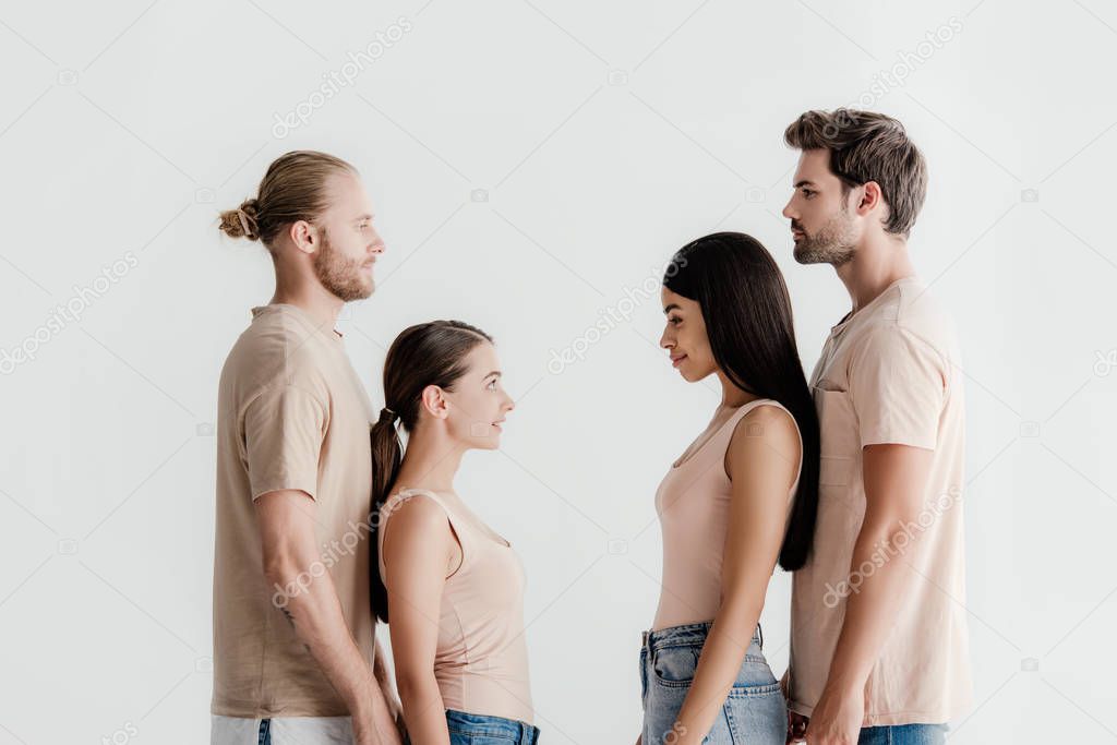 side view of young multicultural men and women in beige outfit standing face to face isolated on white