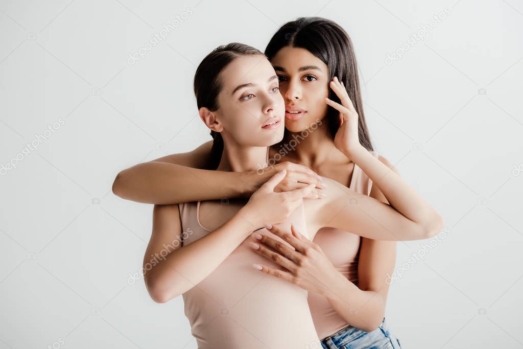 beautiful young multicultural girls in beige outfit tenderly touching each other isolated on white