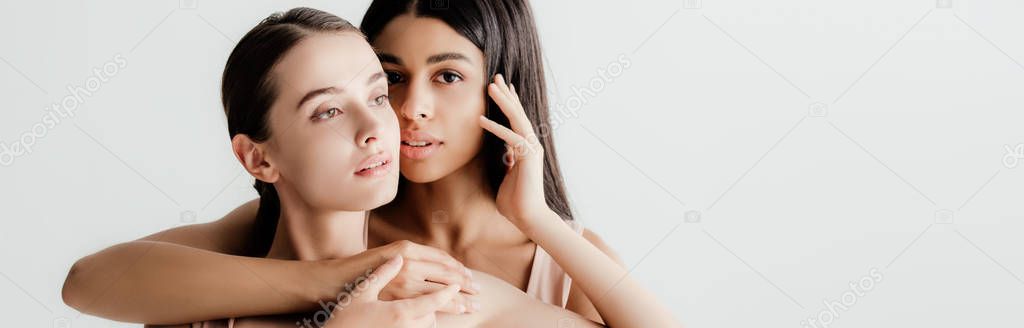 beautiful young multicultural girls in beige outfit tenderly touching each other isolated on white, panoramic shot