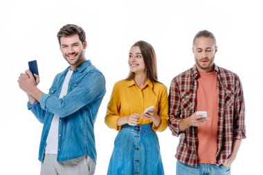 Gülümseyen üç genç arkadaş beyaz üzerinde izole akıllı telefonlar tutuyorlar.