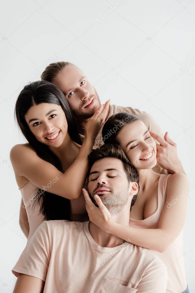 smiling young multicultural men and women in beige outfit posing together and touching faces isolated on white