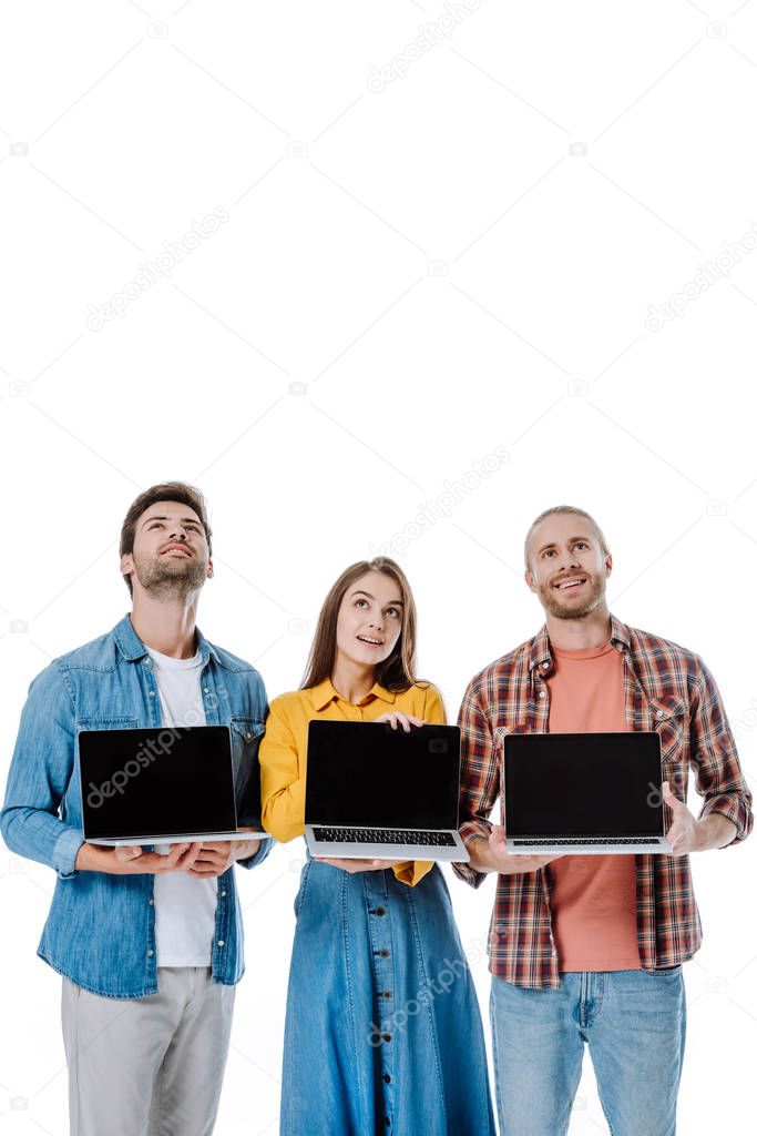 positive young friends holding laptops and looking up isolated on white