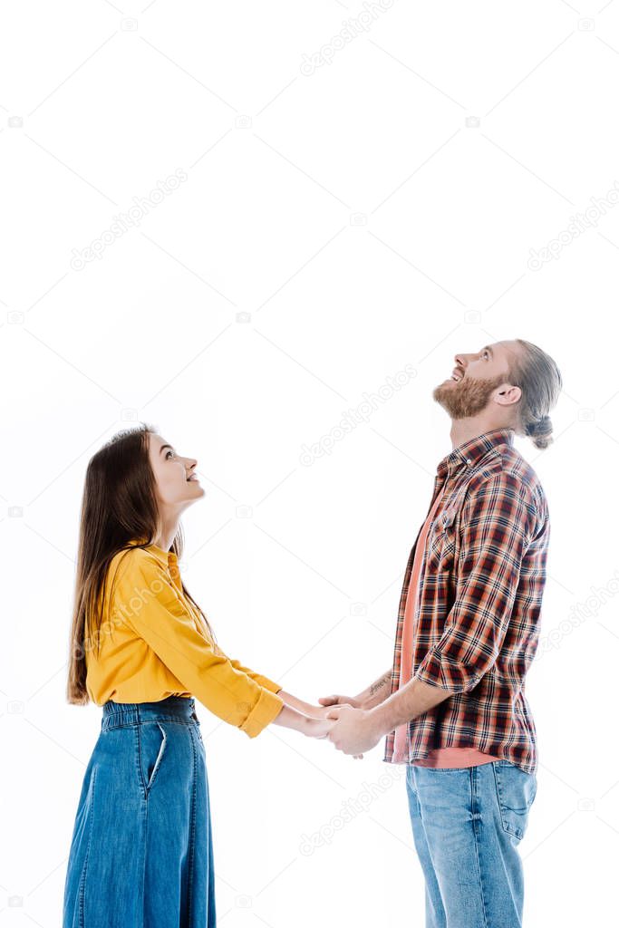 side view of young couple in casual outfit holding hands and looking up isolated on white