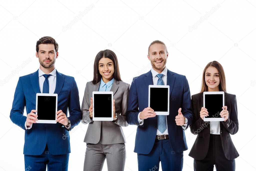 smiling multicultural business people in suits showing digital tablets isolated on white