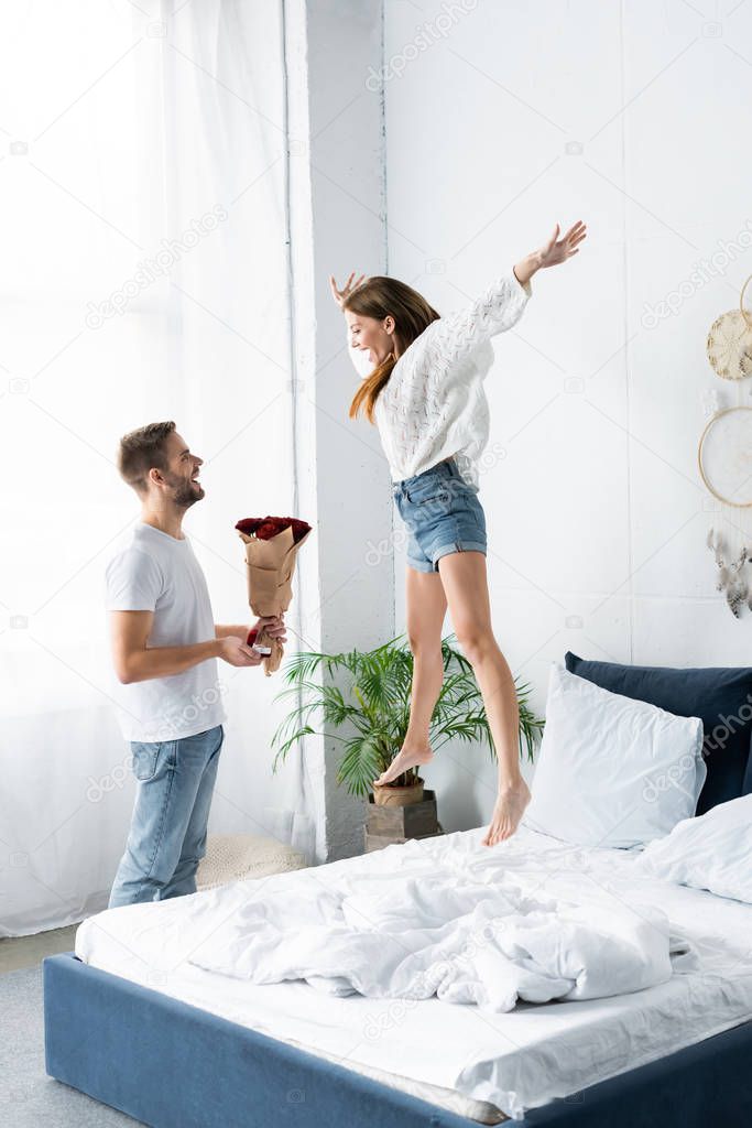 side view of smiling man with bouquet doing marriage proposal to happy woman 