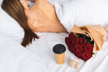 Kağıt bardak ve buketin yanında yatakta uyuyan kadının arka görüntüsü