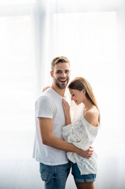 Yakışıklı bir adam dairede çekici ve gülümseyen bir kadına sarılıyor. 