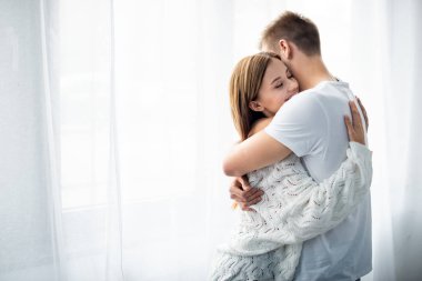 man hugging attractive and smiling woman in apartment  clipart