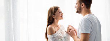 Evinde gülümseyen bir kadınla el ele tutuşan yakışıklı adamın panoramik görüntüsü. 