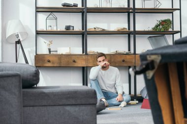 handsome and shocked man obscuring face in robbed apartment  clipart