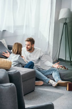 woman and handsome man quarreling and sitting on floor in robbed apartment  clipart