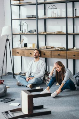 sad woman and handsome man sitting on floor in robbed apartment  clipart