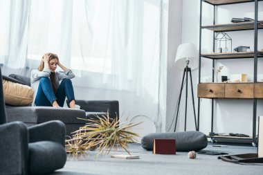 Çekici ve üzgün bir kadın soyulan dairedeki kanepede oturuyor. 