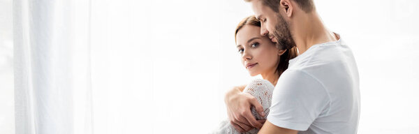 панорамный снимок красивого мужчины, обнимающего привлекательную женщину в квартире
 