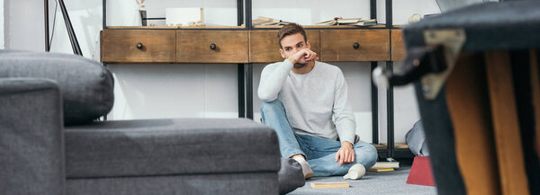 panoramic shot of handsome man sitting in robbed apartment 