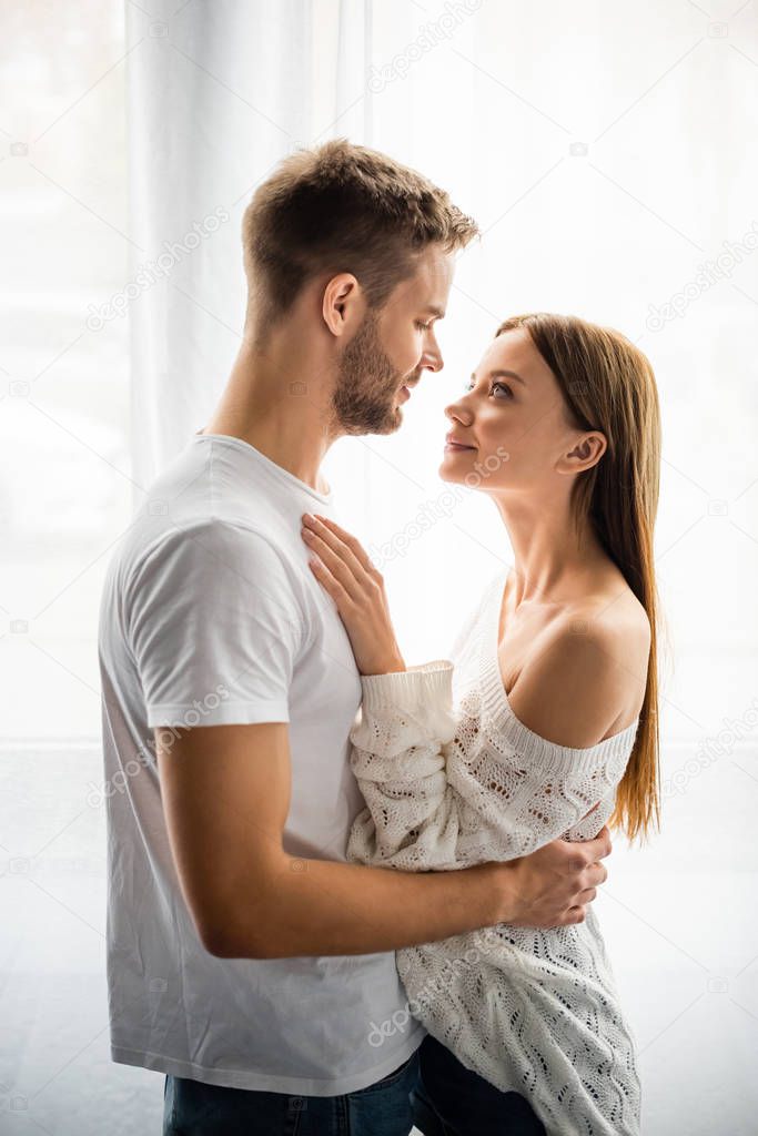 side view of handsome man hugging attractive and smiling woman in apartment 
