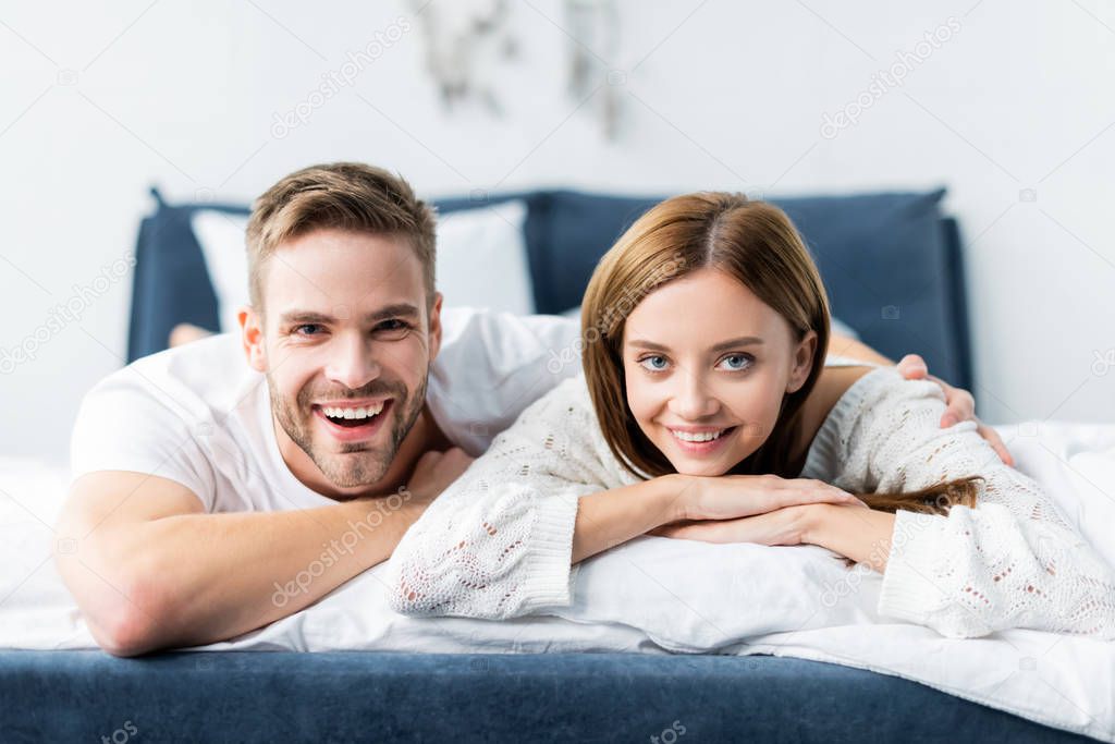 handsome man hugging attractive and smiling woman in apartment 