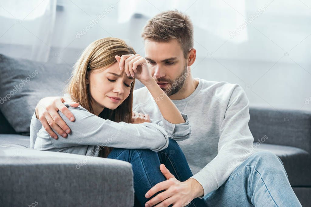 handsome man calming down sad woman in robbed apartment 