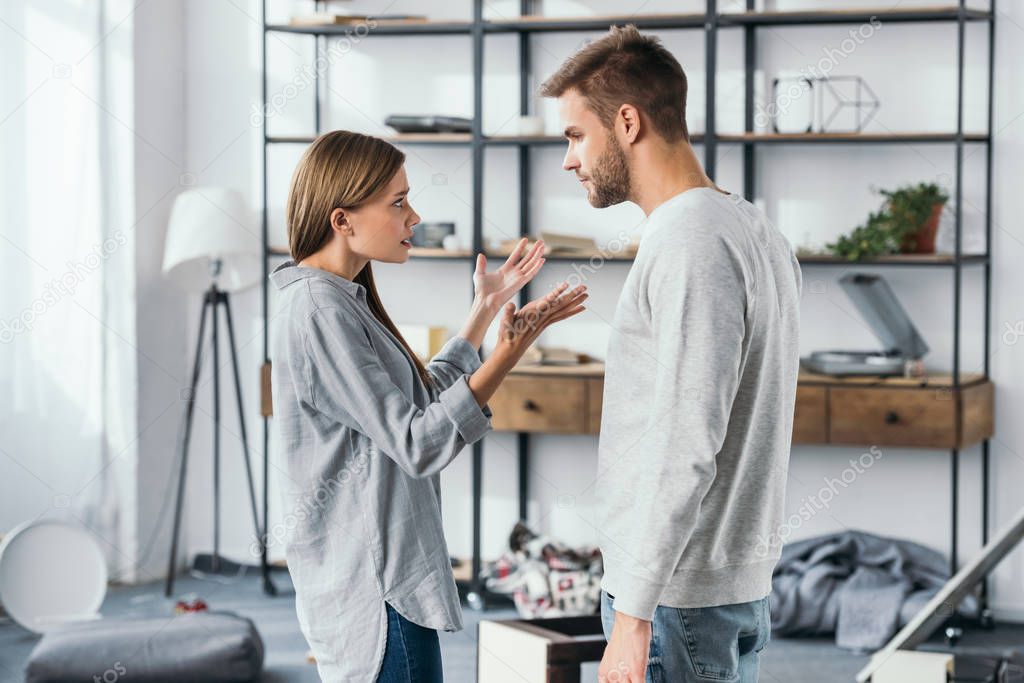 side view of angry woman and handsome man quarreling in robbed apartment 