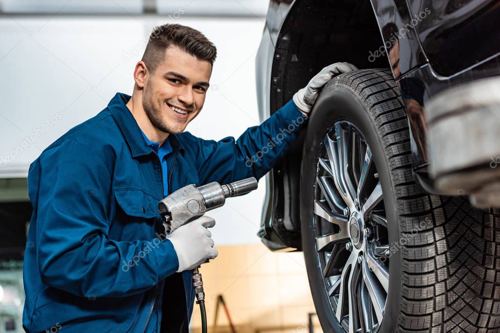 cheerful mechanic looking at camera while holding pneumatic wrench