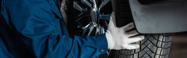 cropped view of mechanic installing wheel on car in workshop, panoramic shot clipart