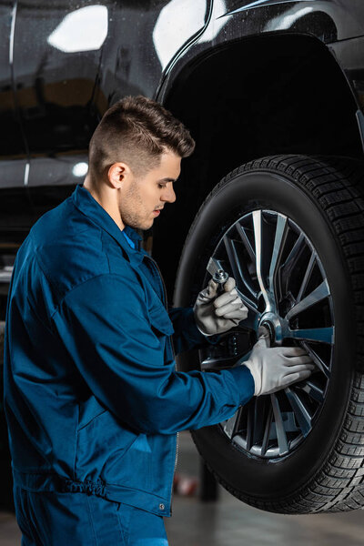 Mechanic looking at screw nut while fixing wheel on car
