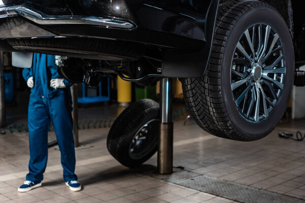 cropped view of mechanic standing near car raised on car lift