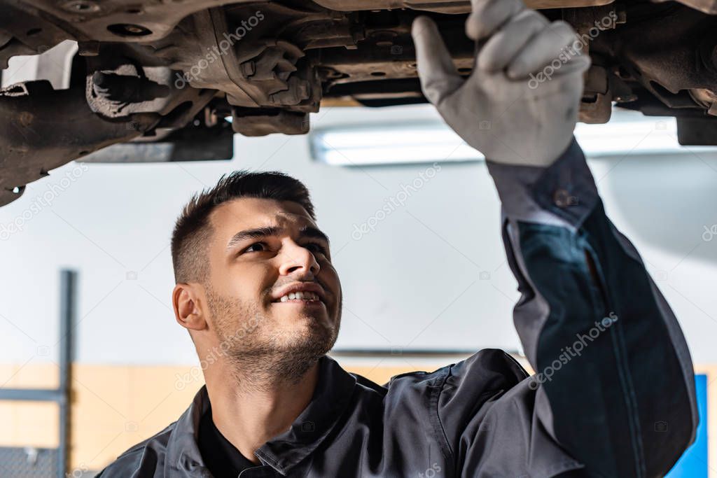 concentrated mechanic examining raised car in workshop