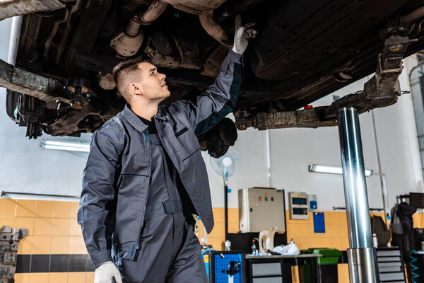 attentive mechanic inspecting bottom of raised car in workshop