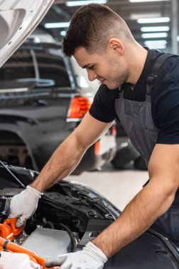 Genç, gülümseyen tamirci araba motoru kompartımanını inceliyor. 