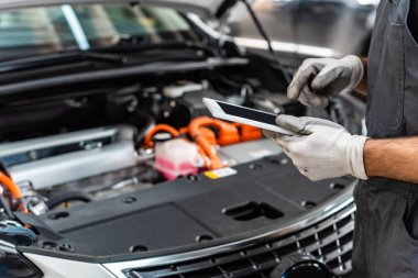 partial view of mechanic using digital tablet near car engine compartment clipart